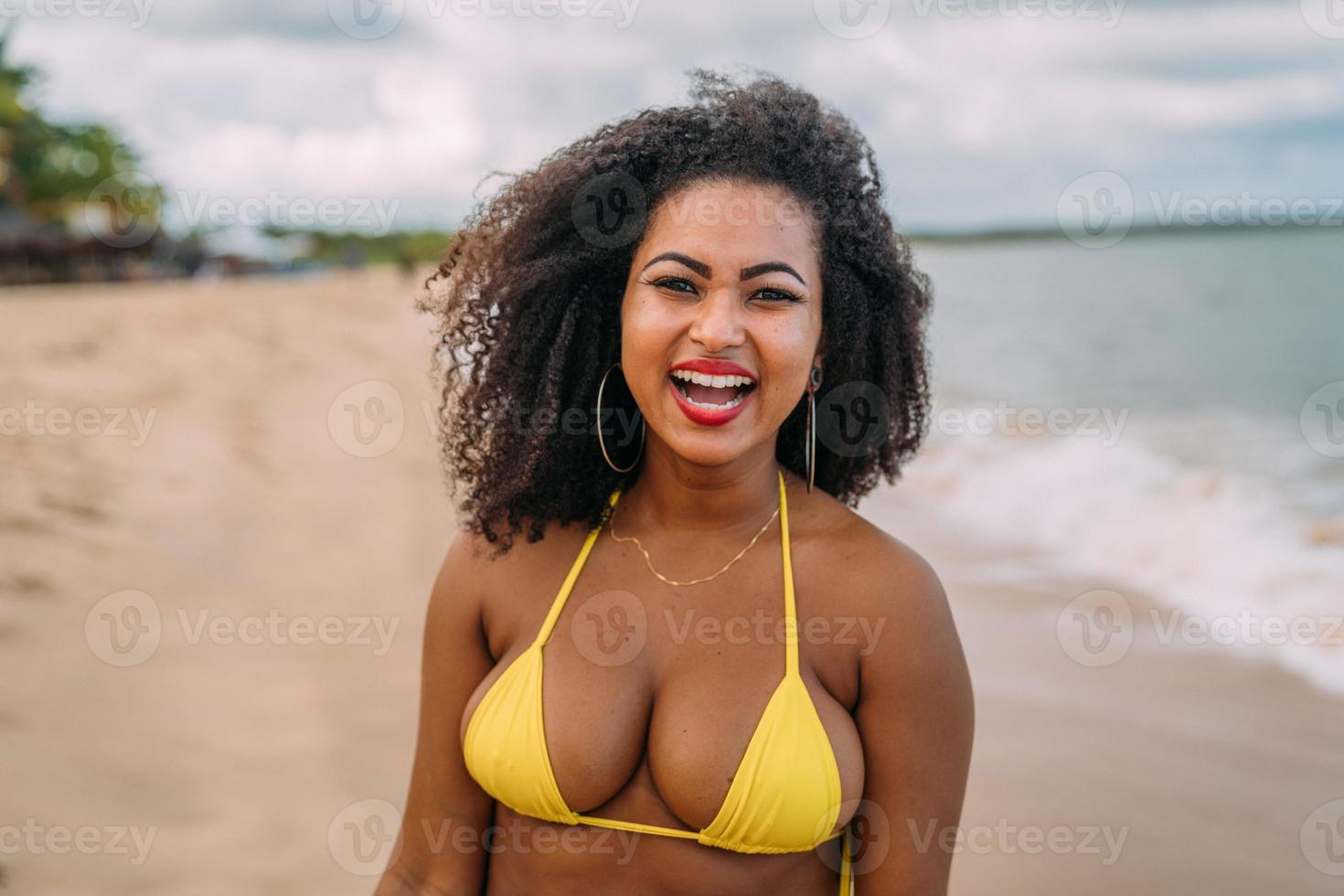 hermosa mujer latinoamericana en bikini en la playa. mujer joven disfrutando de sus vacaciones de verano en un día soleado, sonriendo y mirando a la cámara foto