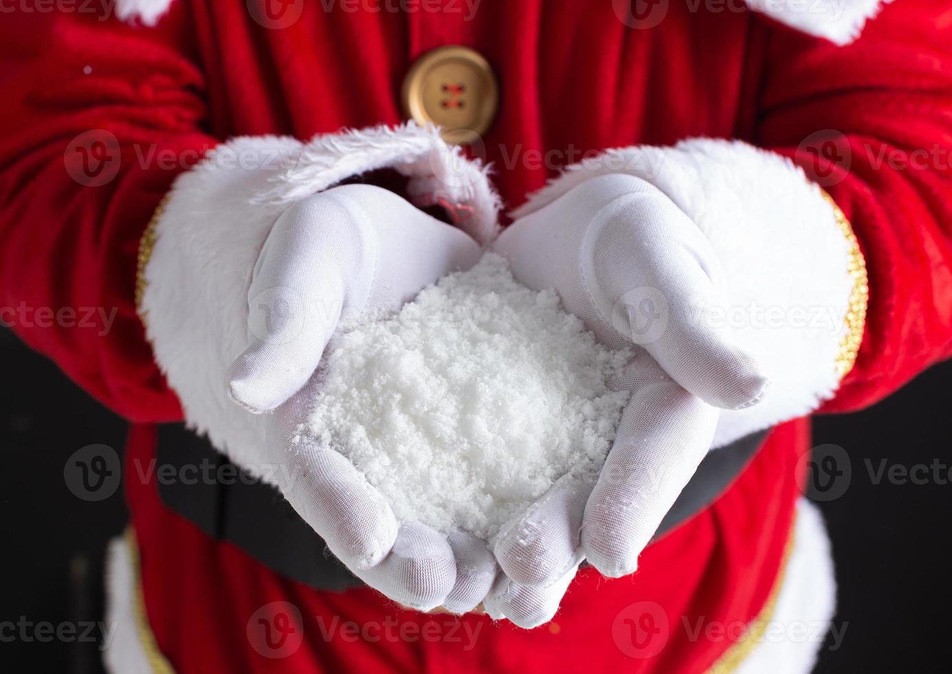 manos de santa sosteniendo un puñado de copos de nieve en sus manos. foto