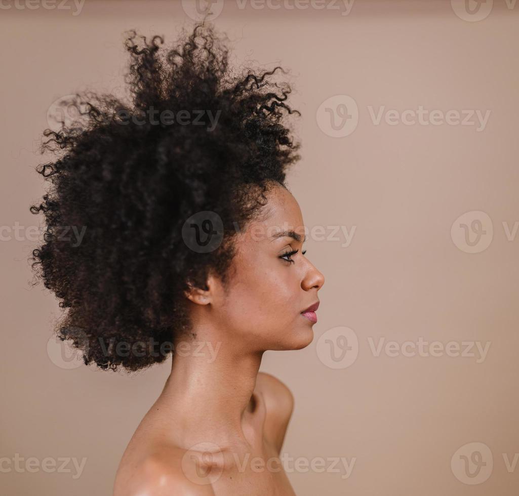 Side a smiling young Latin afro woman. Joy, positive and love. Beautiful african-style hair. Pastel studio background. photo