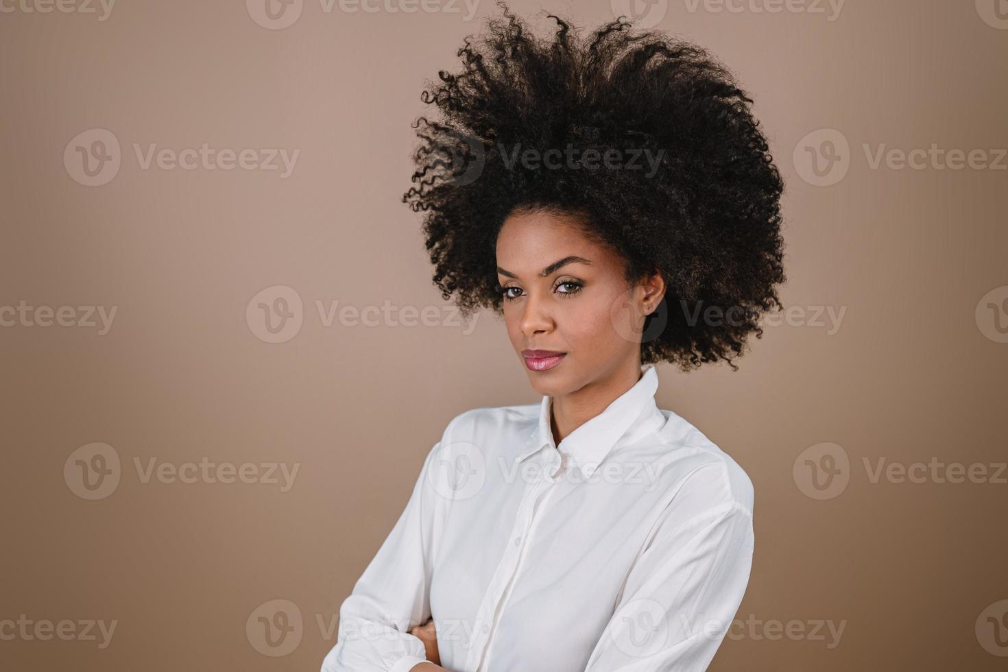 Closeup of a young Latin afro woman crossing arms. Joy, positive and love. Beautiful african-style hair. Pastel studio background. photo