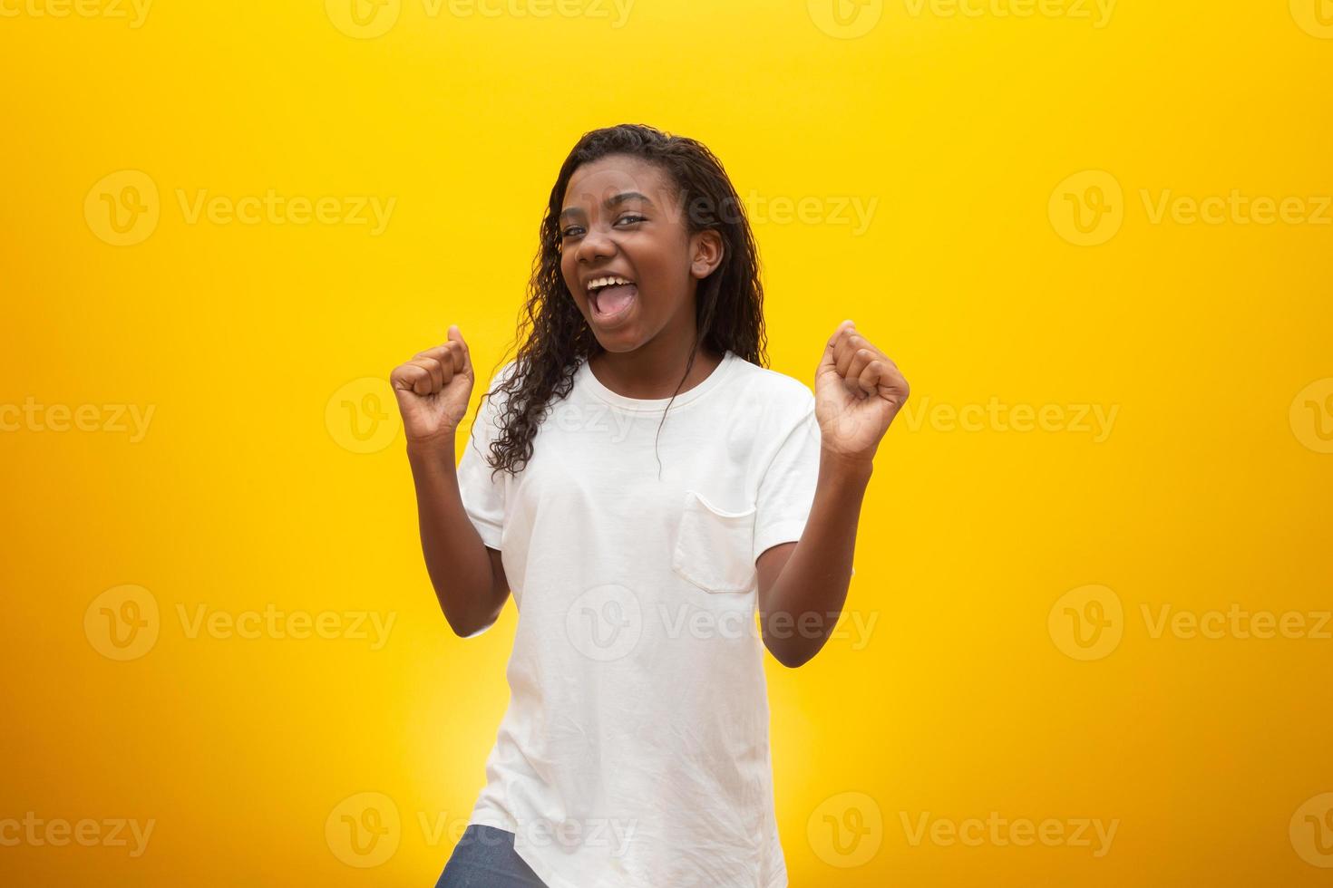 Happy african-american little girl at yellow studio background, copy space. Portrait of beautiful child having fun photo