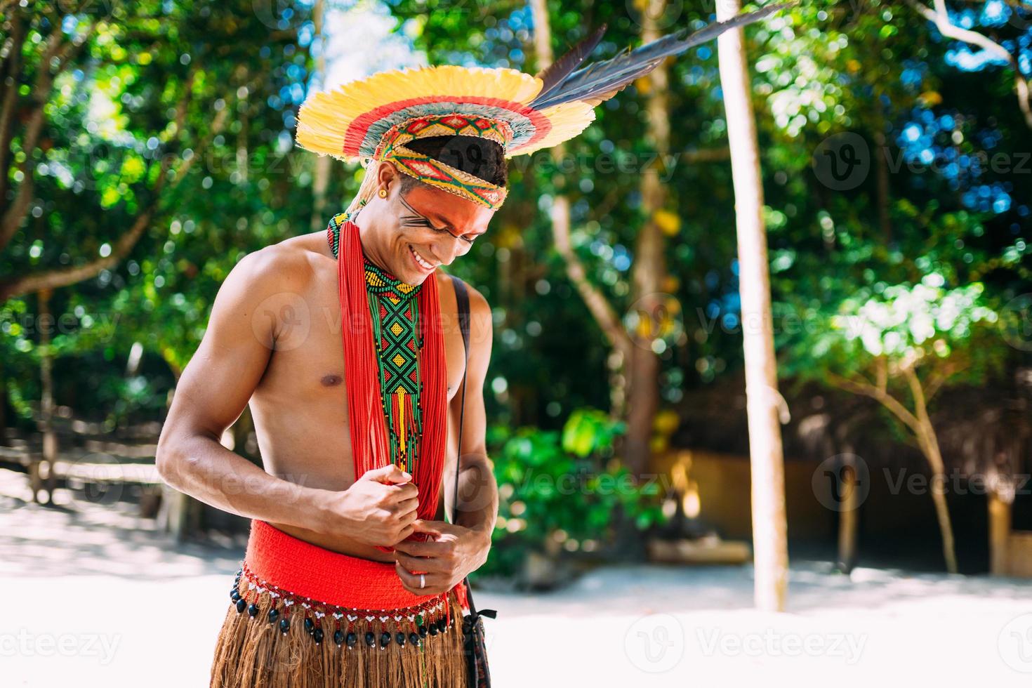 indio de la tribu pataxo con tocado de plumas mirando hacia abajo y sonriendo. indígenas de brasil con pinturas faciales tradicionales. foto
