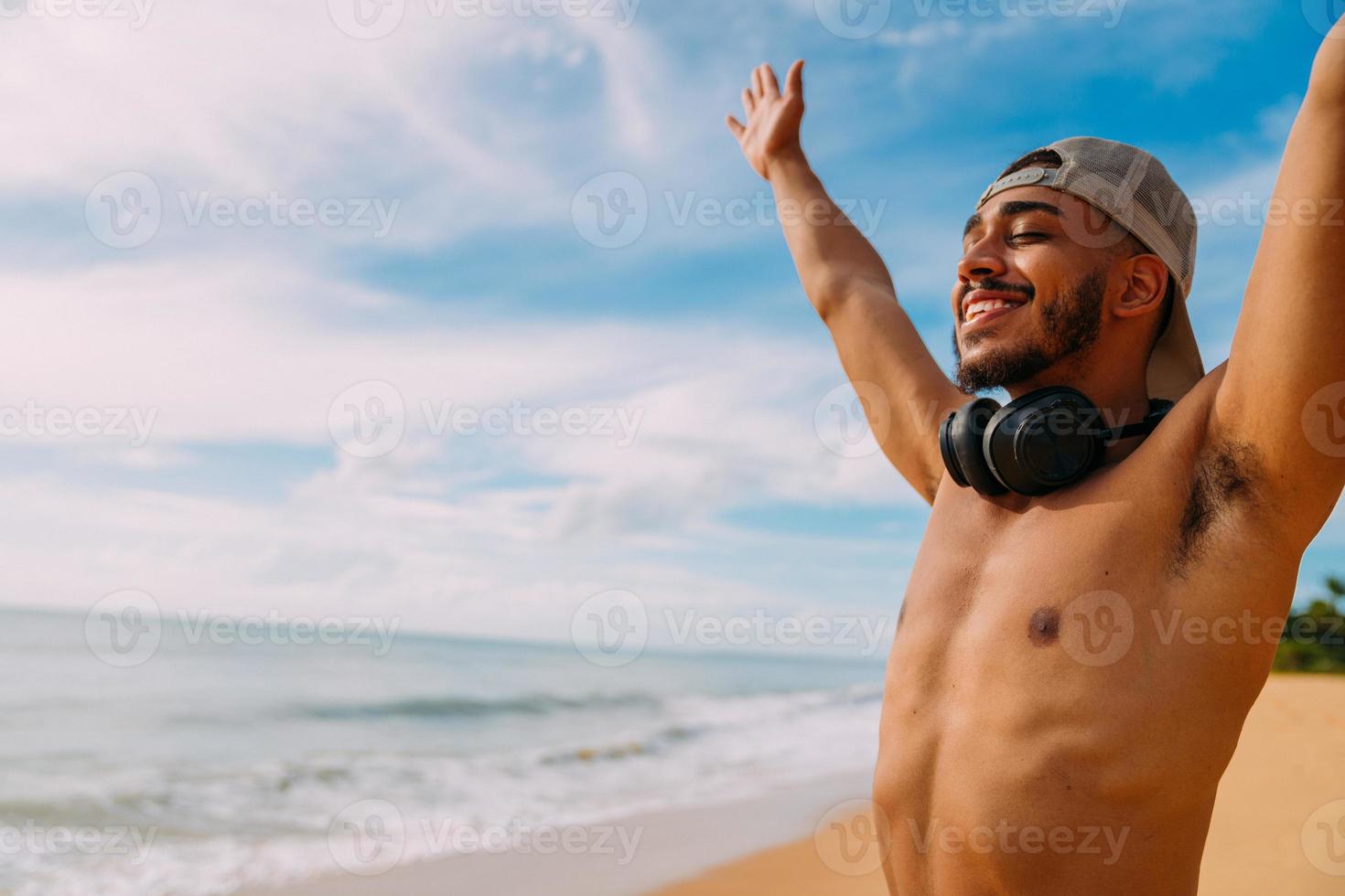 summer holidays, technology and internet concept. smiling and happy latin american man with arms wide open up. man wearing headphone and cap photo