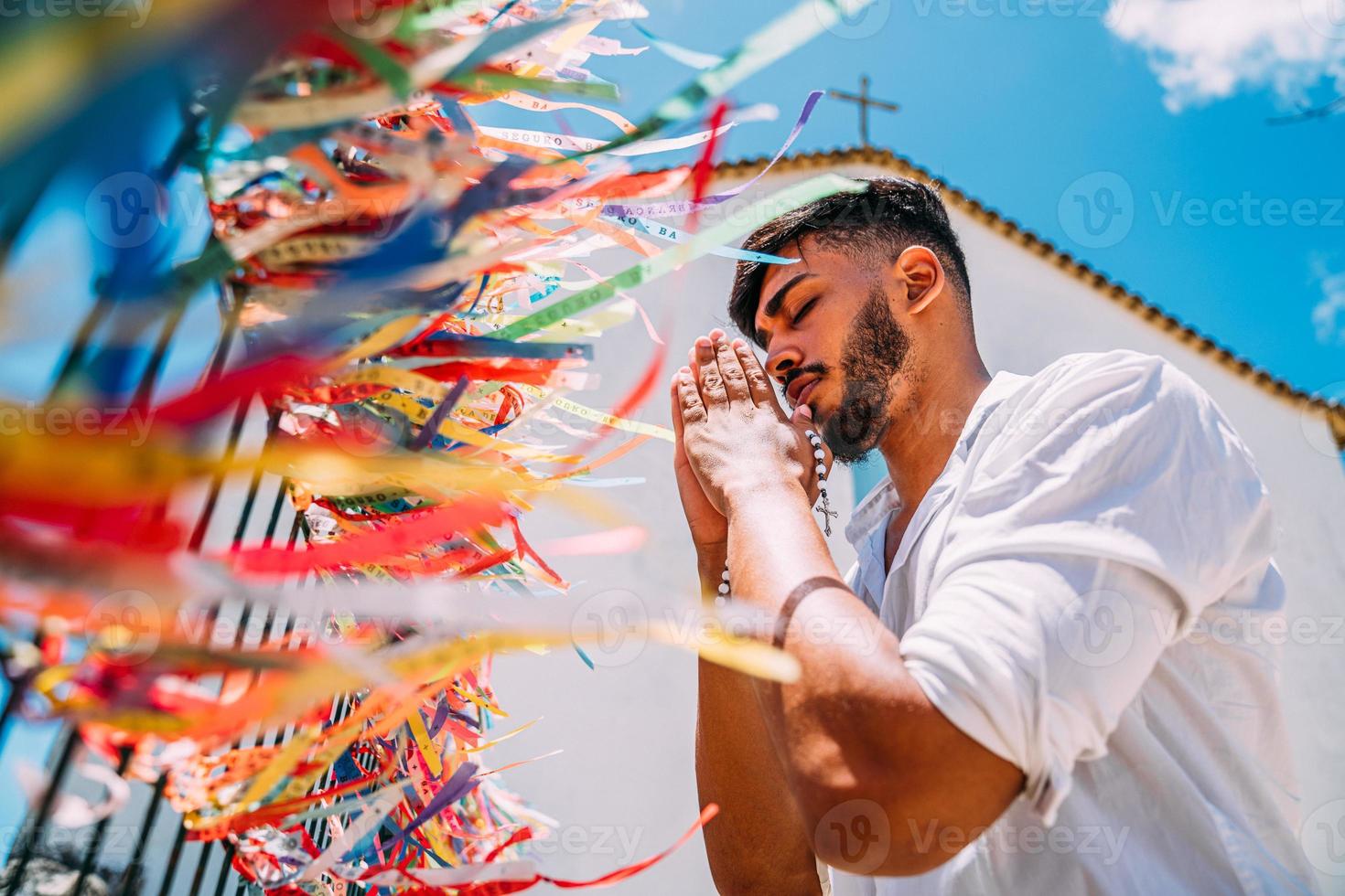 Latin American man placing an order with Brazilian tapes on the fence of a church in Arraial d'Ajuda, Bahia, Brazil. Focus on colored ribbons photo
