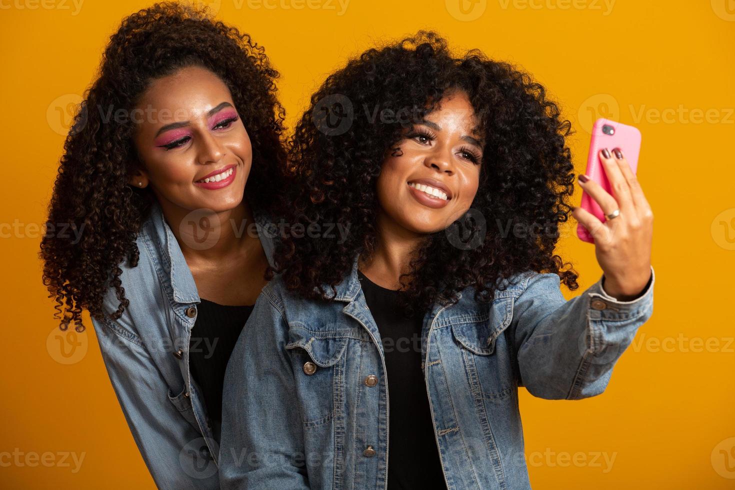 dos chicas afroamericanas tomando fotos selfie con su teléfono celular con fondo amarillo