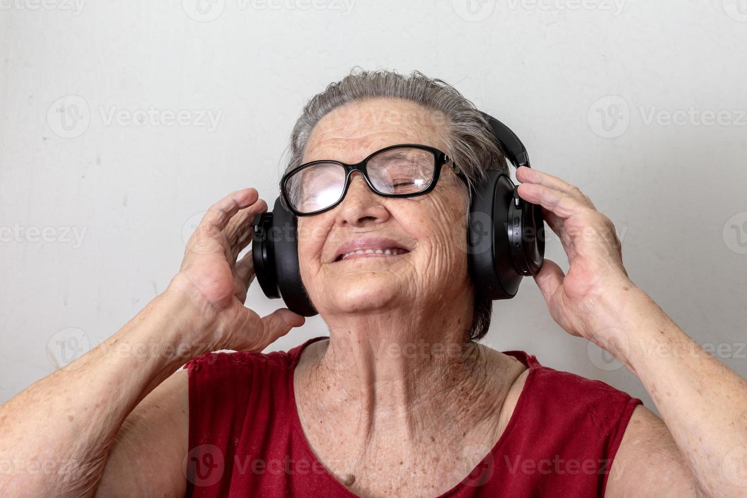 divertida anciana escuchando música y bailando sobre fondo blanco. anciana con gafas bailando música escuchando en sus auriculares. foto