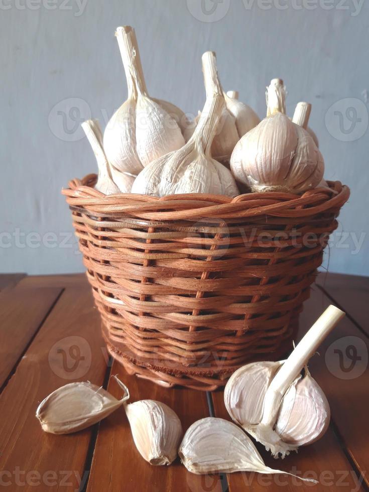 Closeup garlic are in the wicker basket on the wooden table photo