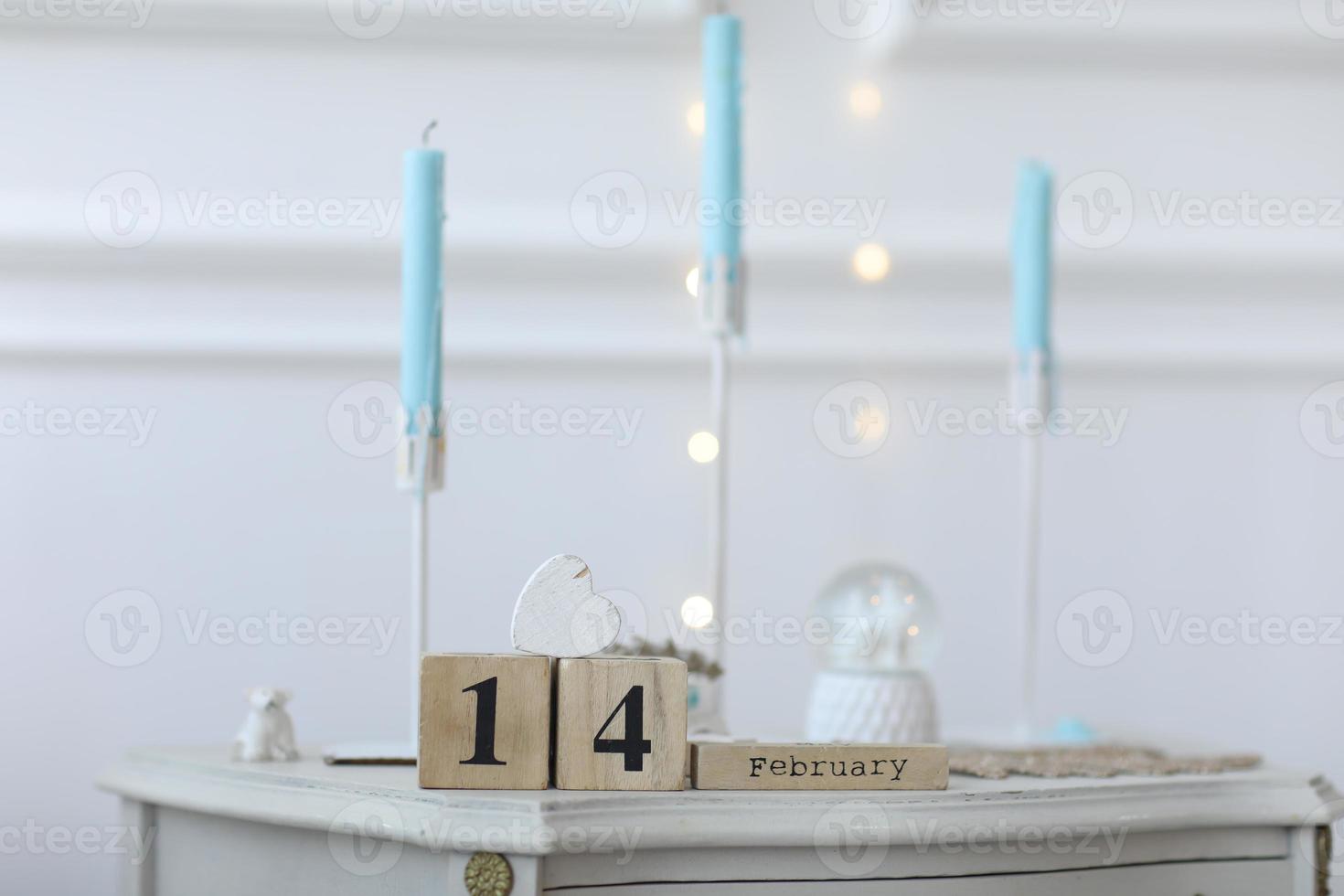 concepto de día de san valentín. calendario de cubo de madera con fecha del 14 de febrero con corazón de madera blanca desde arriba sobre la mesa. candelabros blancos con fondo de velas azules y bokeh con luz foto