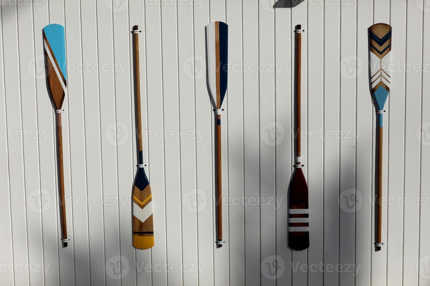 four colourful wooden paddles hangs on a white wall. canoe oars for active water sport. holiday vacation. High quality photo