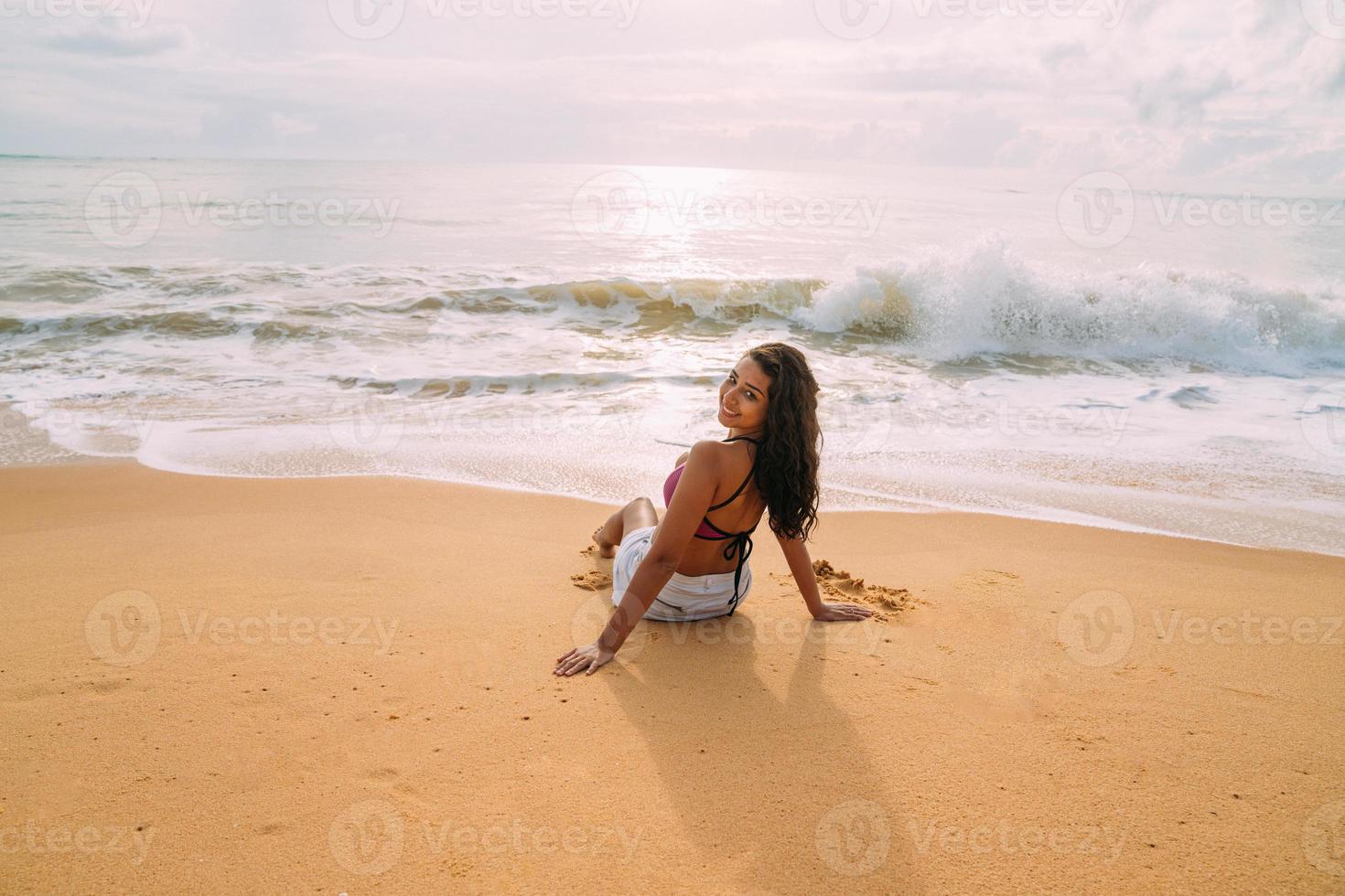 silueta de mujer joven en la playa. mujer latinoamericana sentada en la arena de la playa mirando al cielo en un hermoso día de verano foto