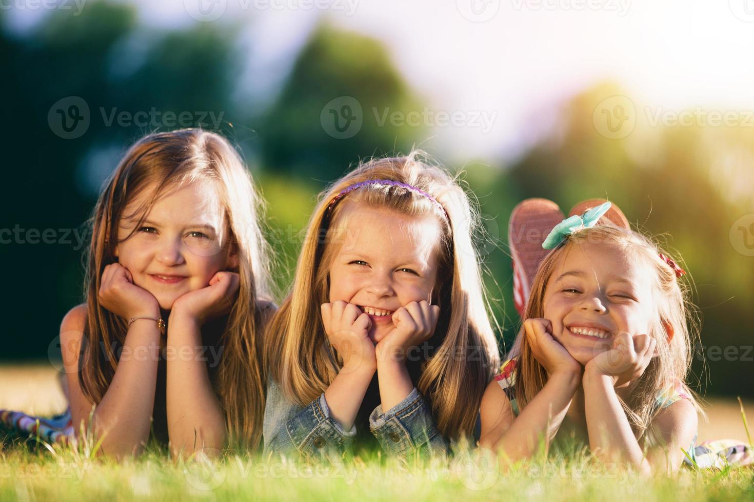 Three smiling little girls laying on the grass in the park. photo