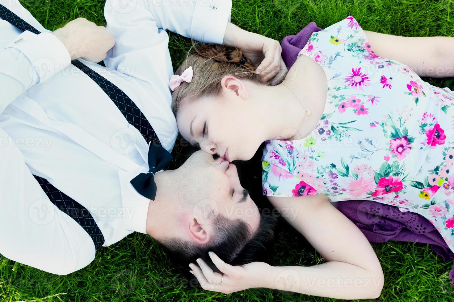 feliz pareja enamorada besándose mientras está acostada en la hierba de verano foto