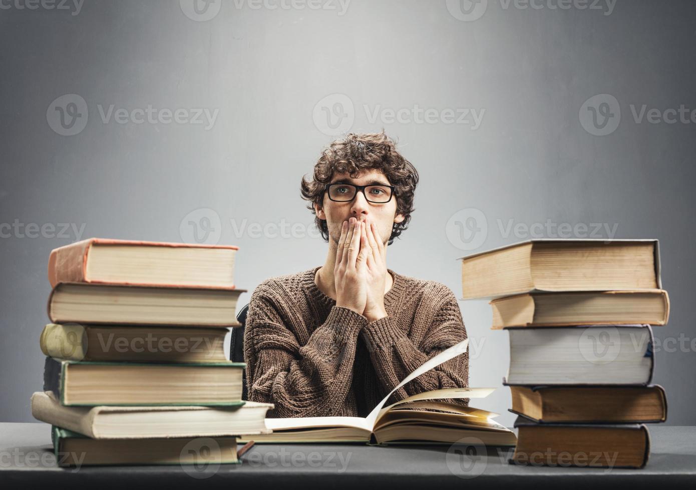 Pensive man sitting by the piles of books. photo