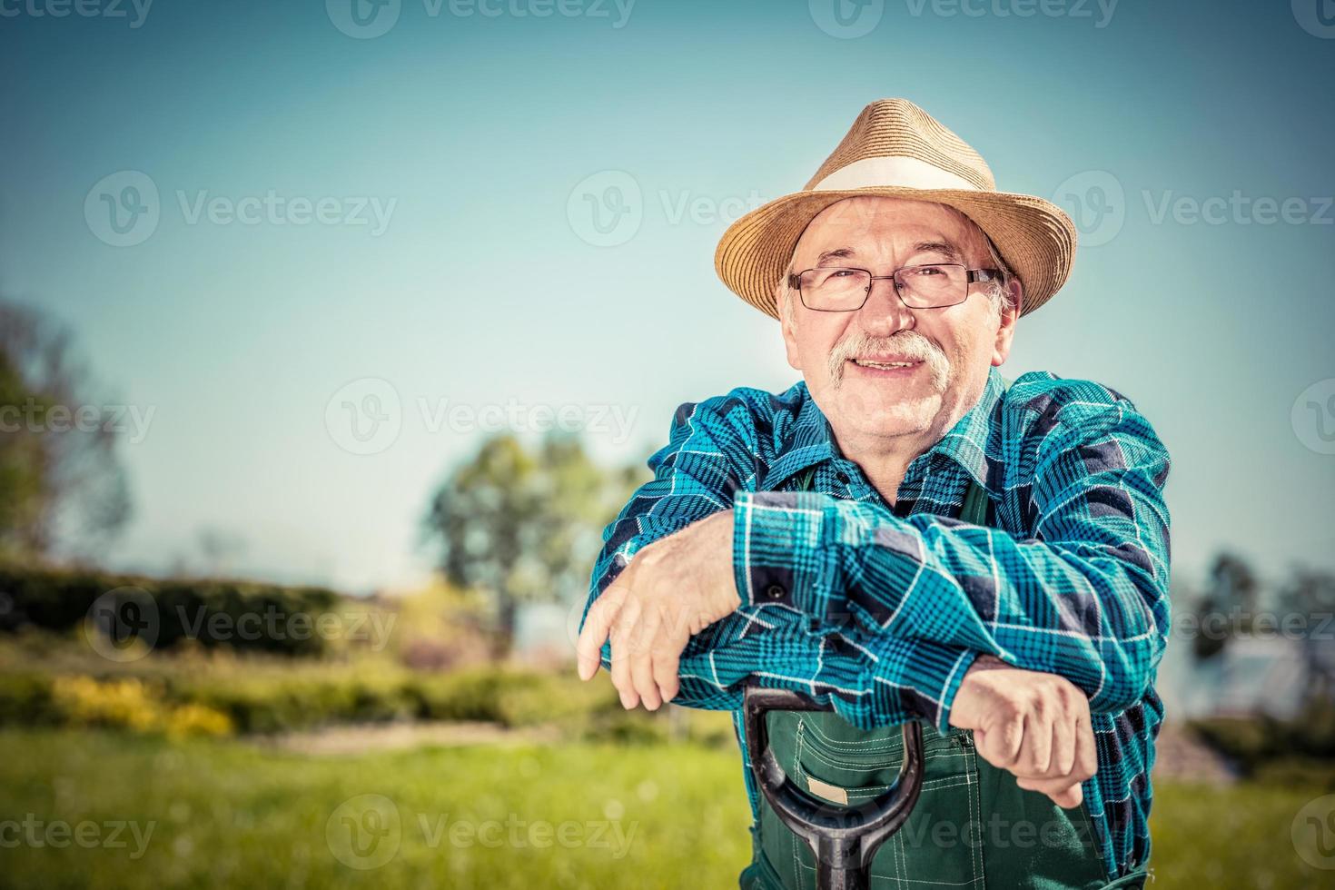 retrato de un jardinero senior parado en un jardín con una pala. foto