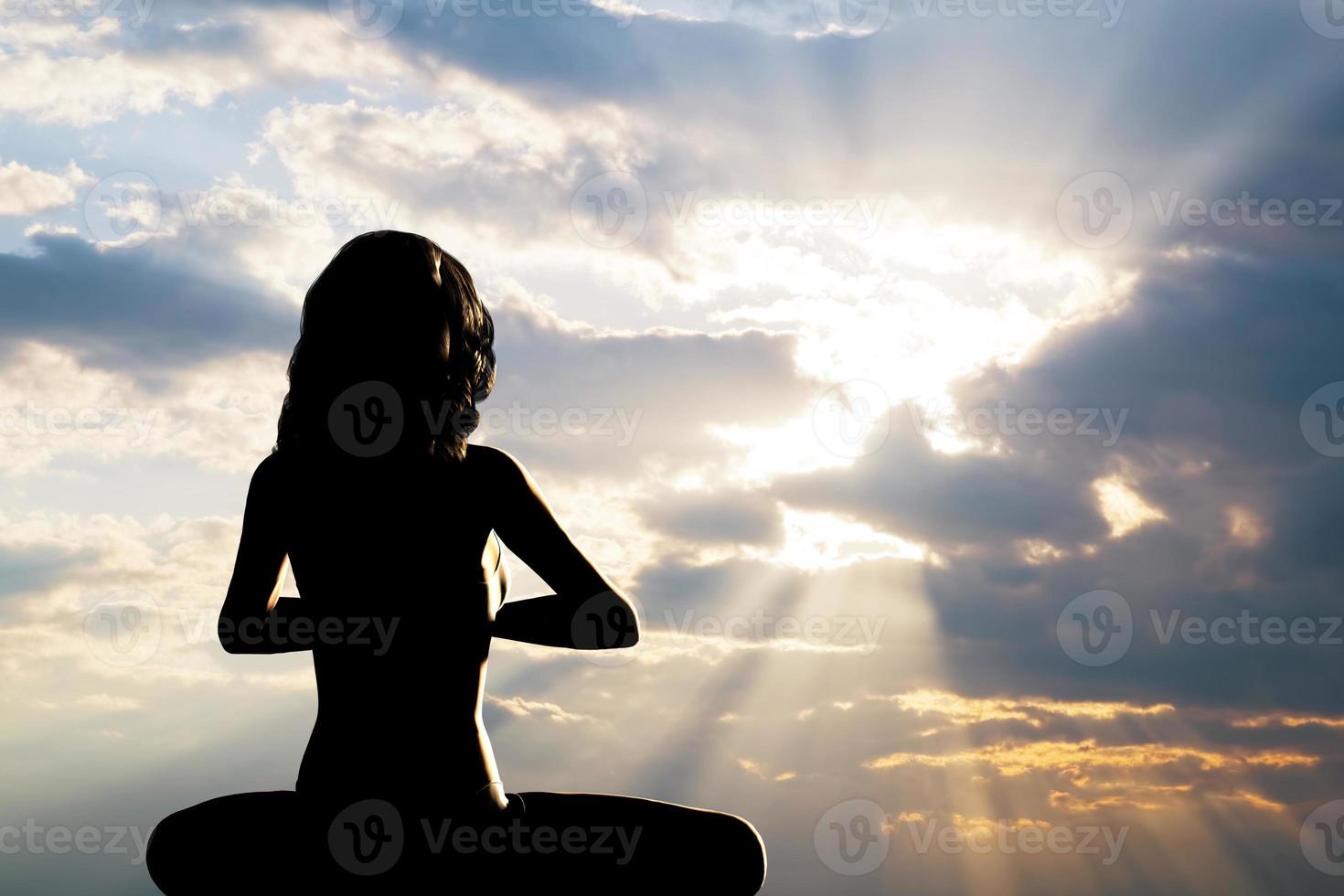 A silhouette of a woman sitting in yoga position, meditating against sunset sky. photo