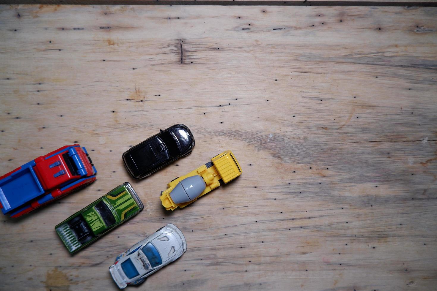 several toy cars lined up neatly on the wood. toy cars photographed  from above. some toy cars on the bottom left. photo