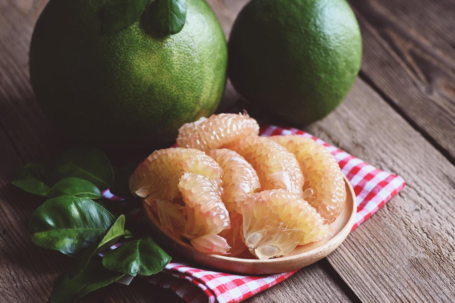 fresh green pomelo peeled and leaf frome pomelo tree , pummelo , grapefruit in summer tropical fruit  in thailand , pomelo fruit on wooden plate background photo