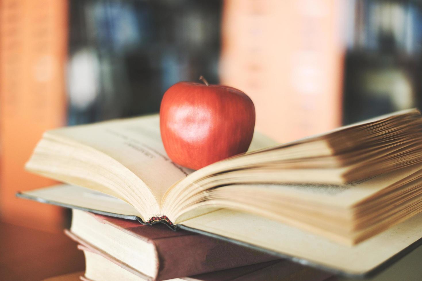 Books on the table in the library - Education learning old book stack on wood desk and blurred bookshelf room background with apple on open book , back to school concept photo