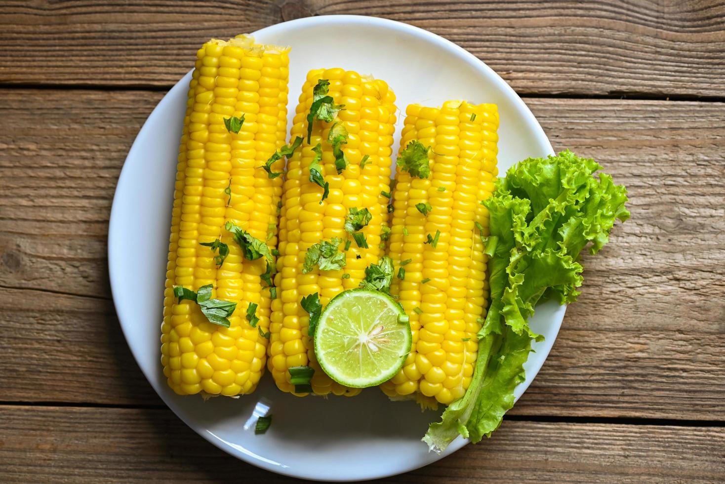 sweet corn cooked on white plate background, sweet corn food with salad vegetable lime coriander and lettuce, ripe corn cobs steamed or boiled sweetcorn for food vegan dinner or snack photo