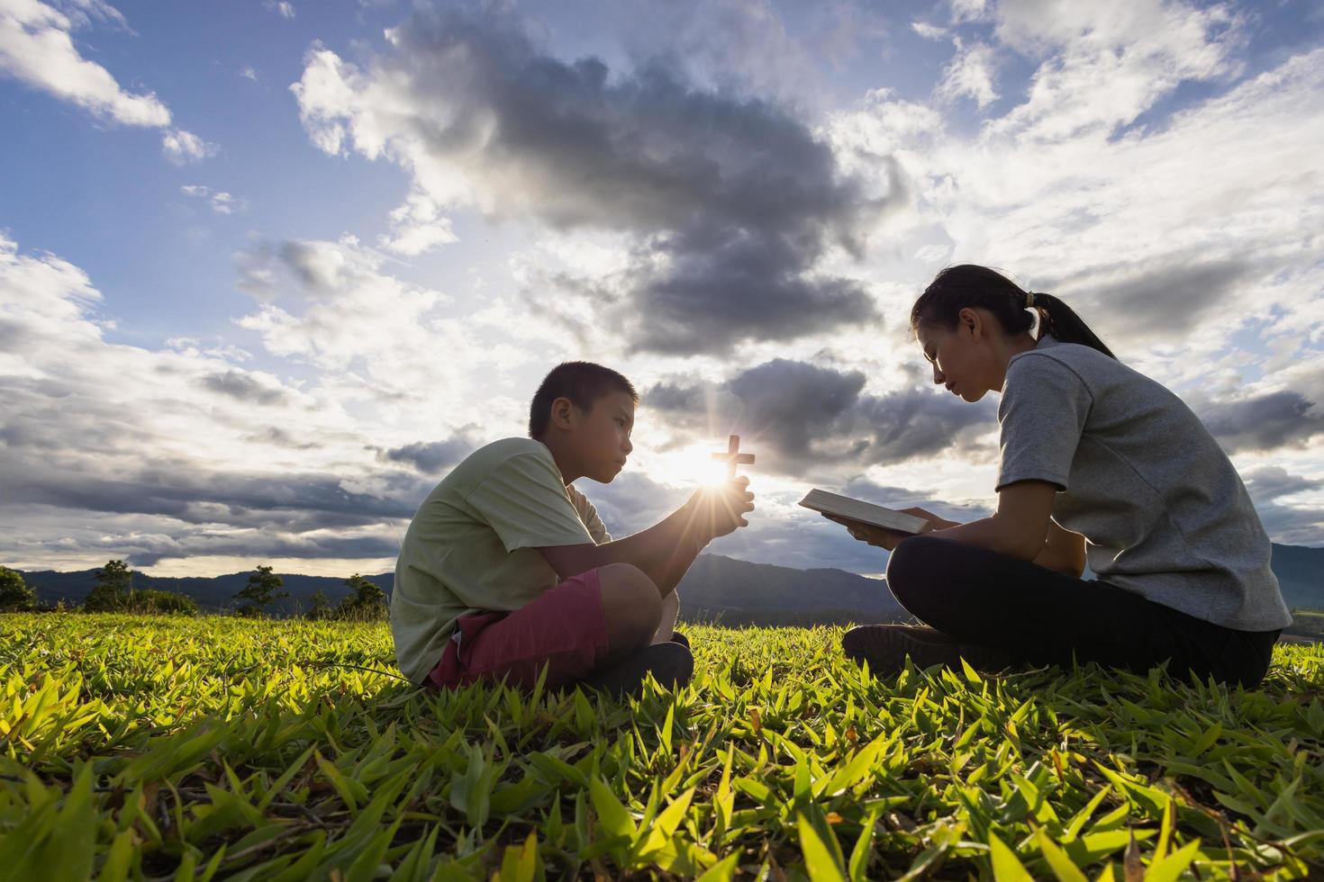 Little boy with mother praying and reading bible in the morning on the mountain with Christian concept copy space. photo