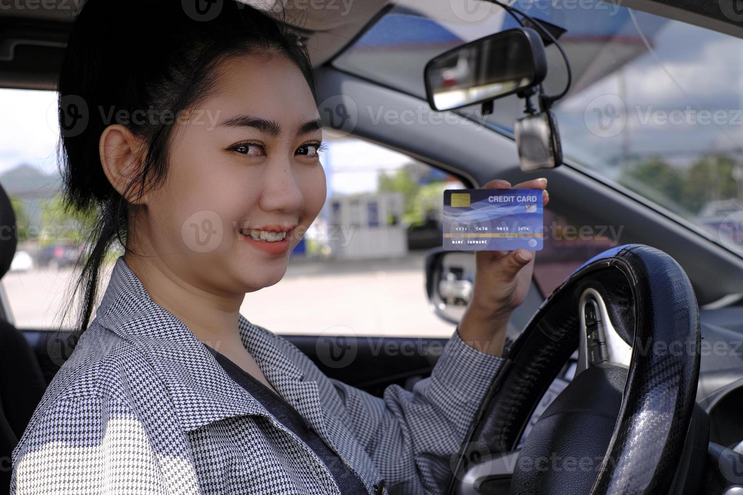 Happy beautiful Asian woman sitting inside her car showing credit card  payment at a gas station photo