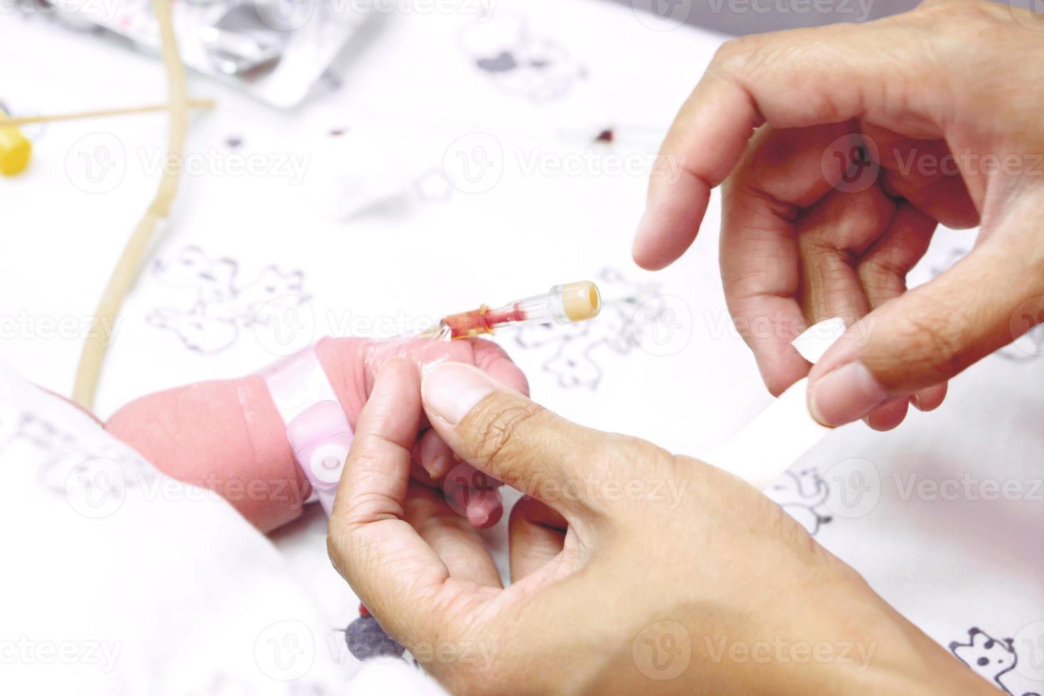 The nurse hands is stabbing injection plug with use a medical tape to attach the needle to the baby's hand and wounding. photo
