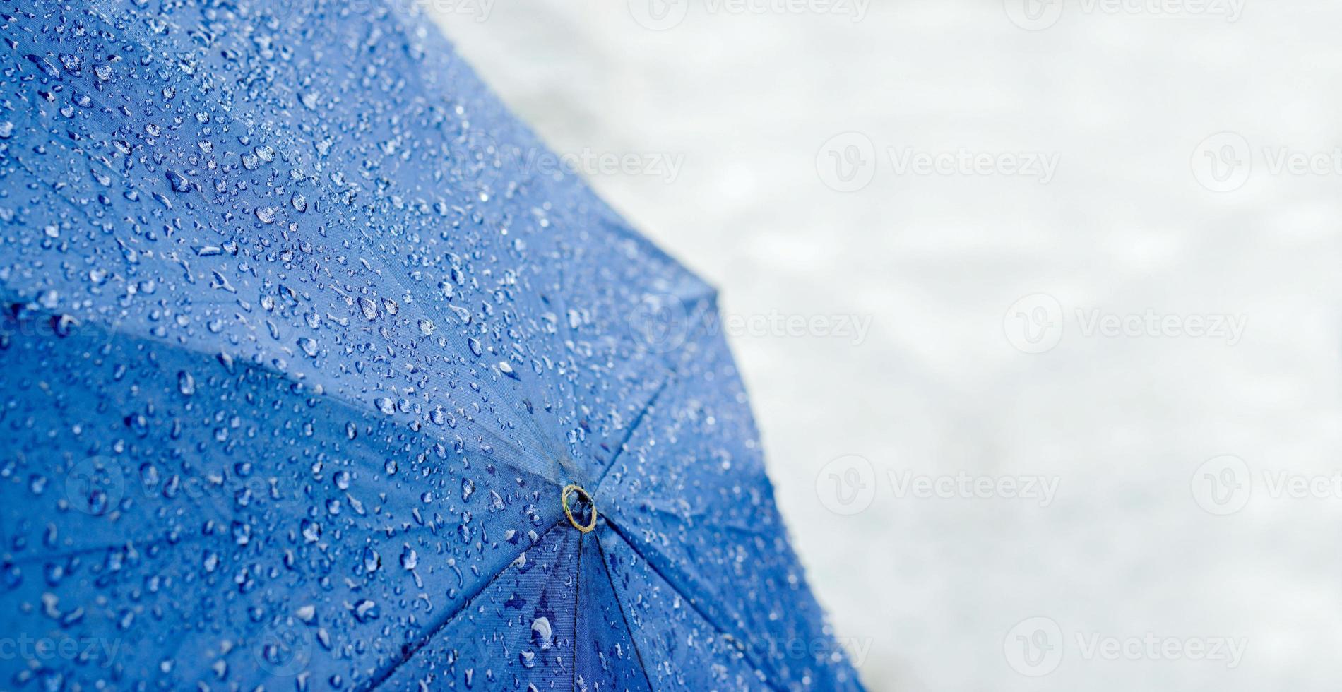 Wide screen of raindrops on blue umbrella with blurry of road on rainy day. photo