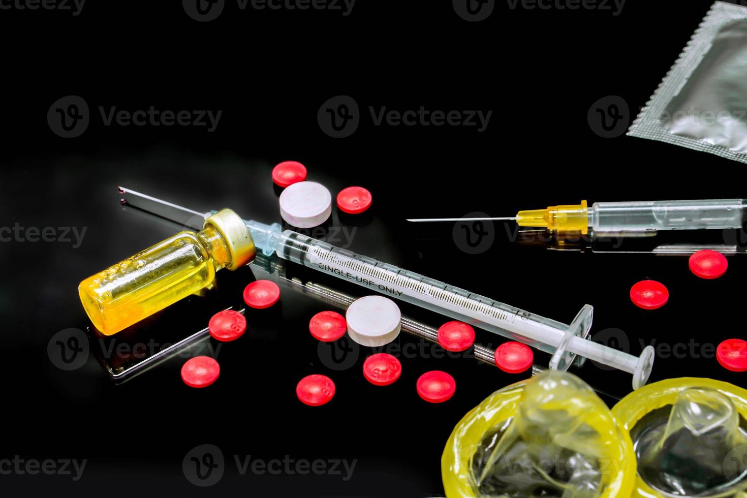 Vaccines in vial,  white and red  medicines with a plastic syringe and condoms isolate on black background. Sample of what caused the HIV infection. and The condom is to prevent infection. photo