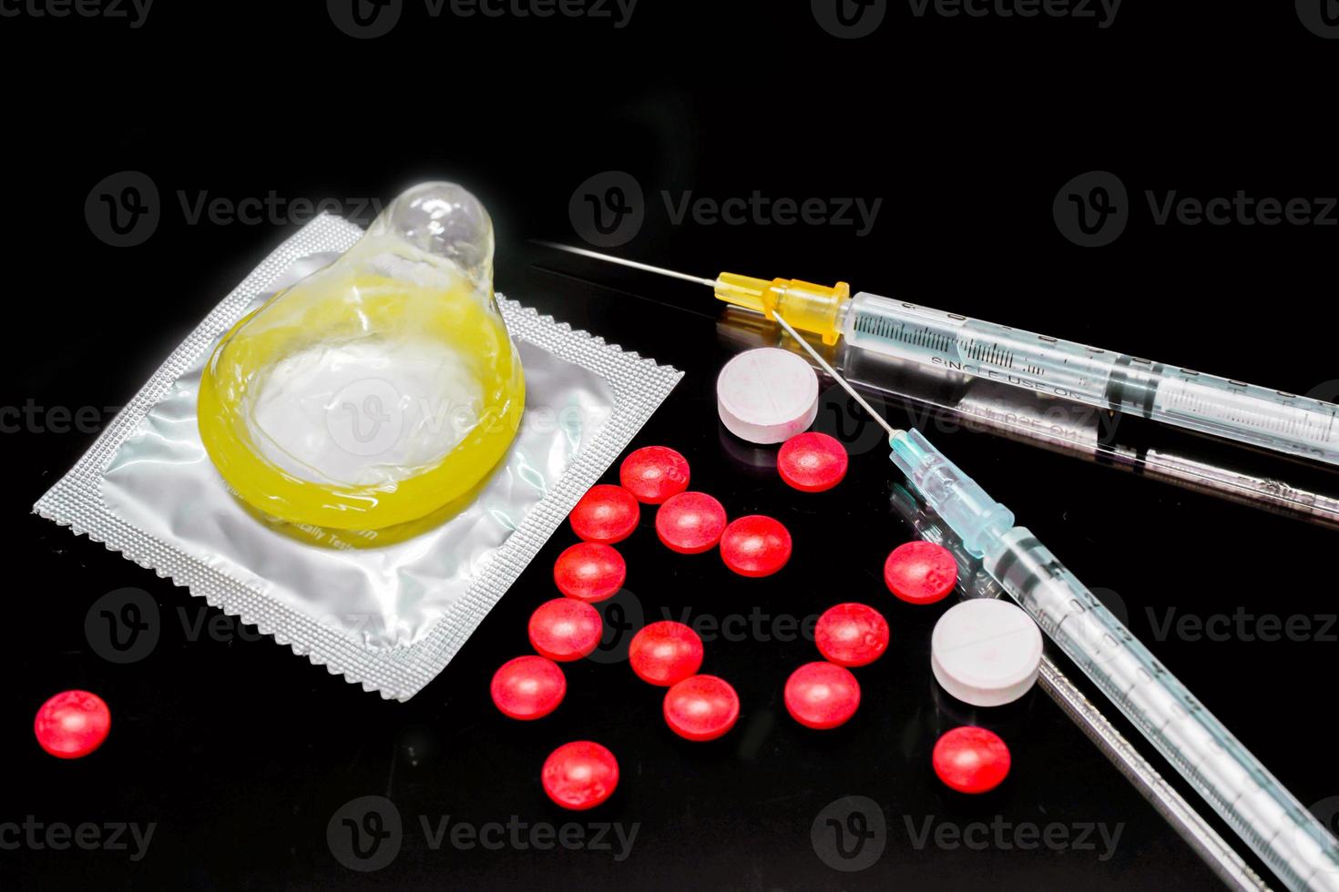 White and red medicines with a plastic syringe and condom isolate on black background. Sample of what caused the HIV infection. and The condom is to prevent infection. photo