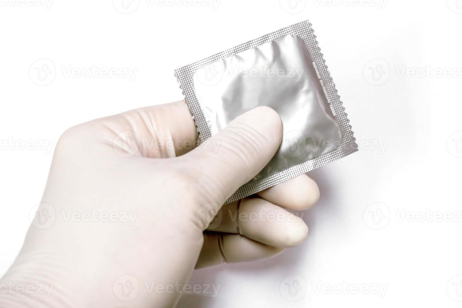 Doctor hand in medical latex glove picking up a condom in package on white background. photo