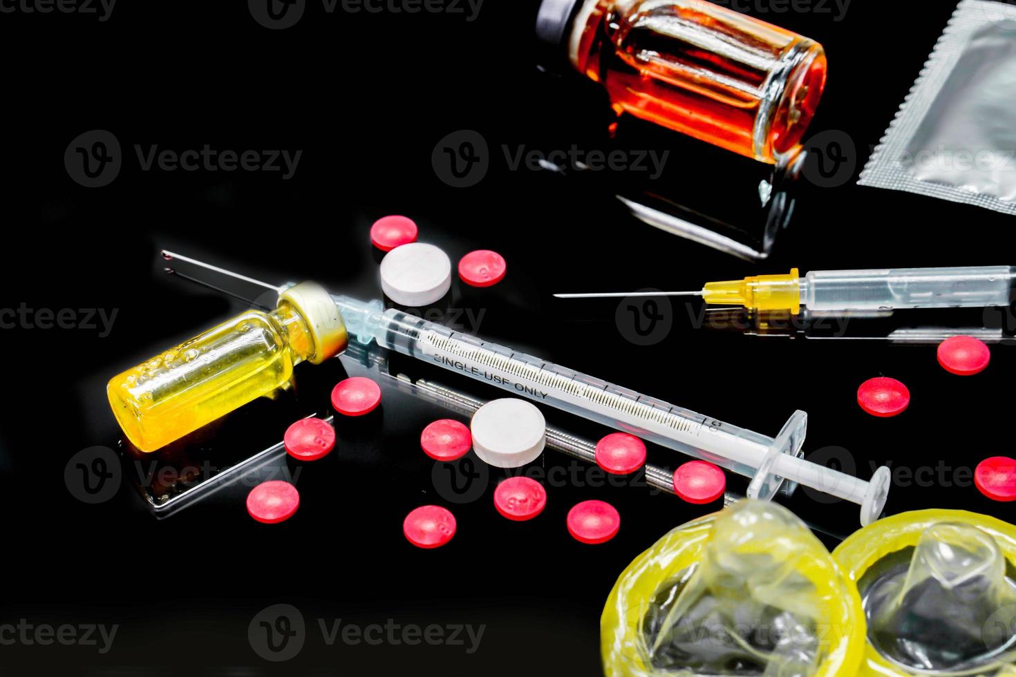 Vaccines in vial,  white and red  medicines with a plastic syringe and condoms isolate on black background. Sample of what caused the HIV infection. and The condom is to prevent infection. photo