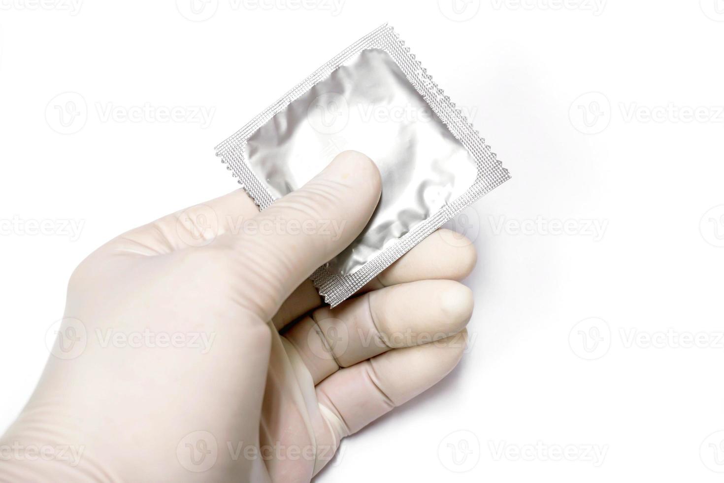 Doctor hand in medical latex glove picking up a condom in package on white background. photo