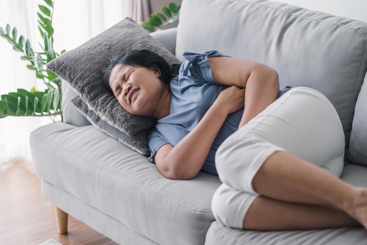 mujer que sufre de dolor de estómago acostada en el sofá de casa. dolor abdominal, gastritis, regla, menstruación. foto