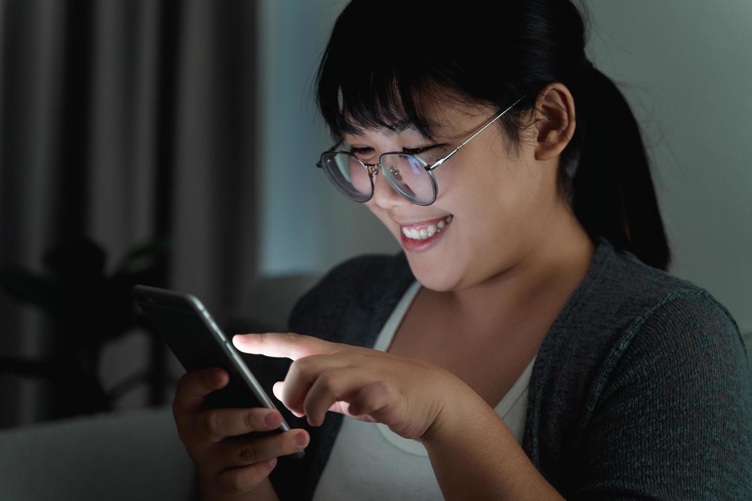 Woman using mobile phone and sitting on the couch in the dark living room at night. photo