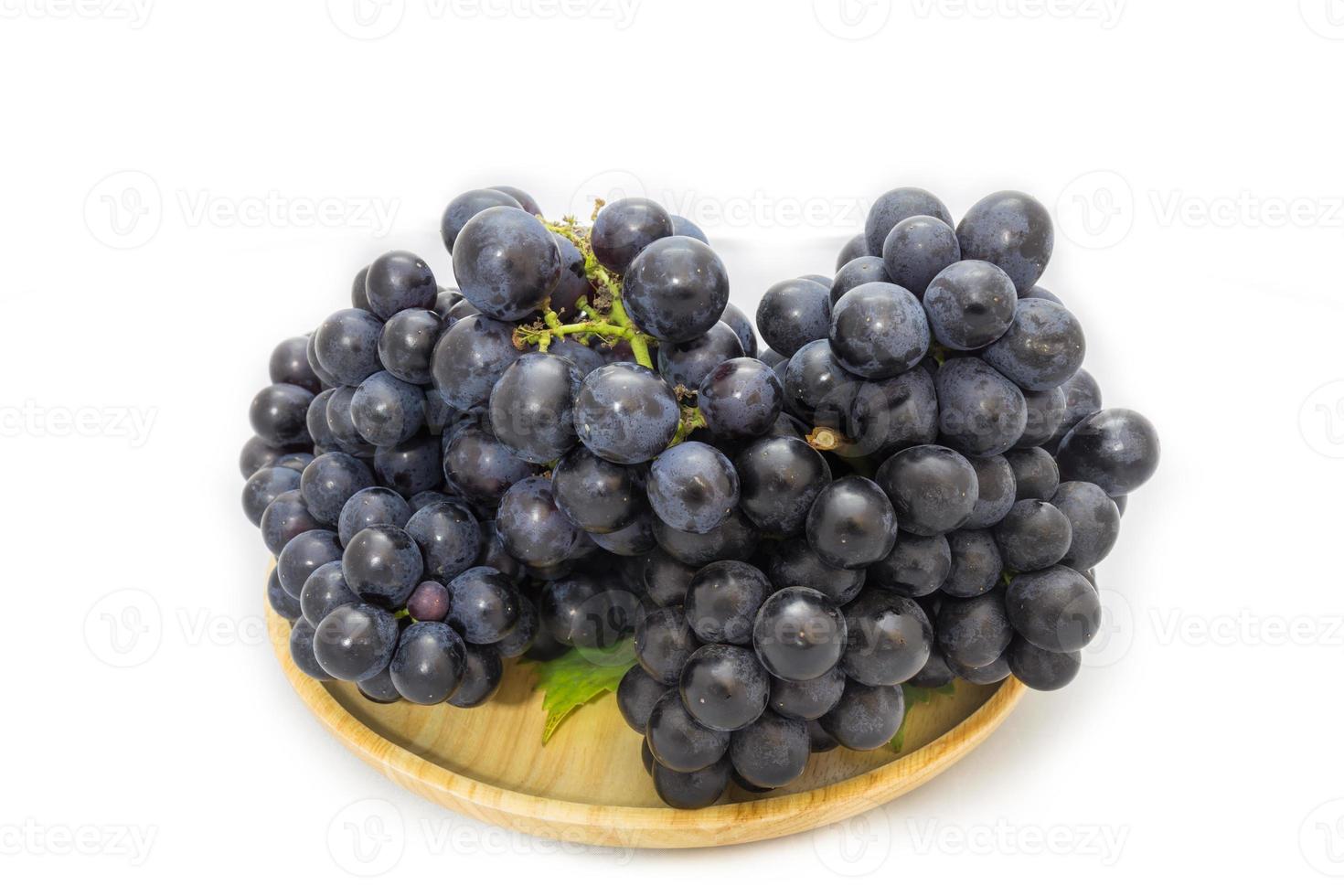 Black grapes bunch isolated on wooden plate and white background with green leaf package design element photo