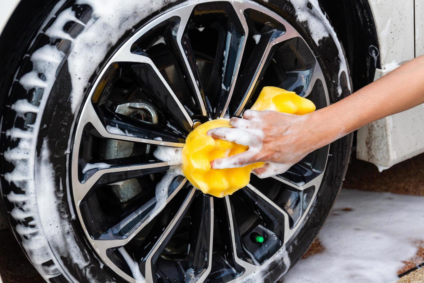 Woman hand with yellow sponge washing wheel modern car or cleaning automobile. Car wash concept photo