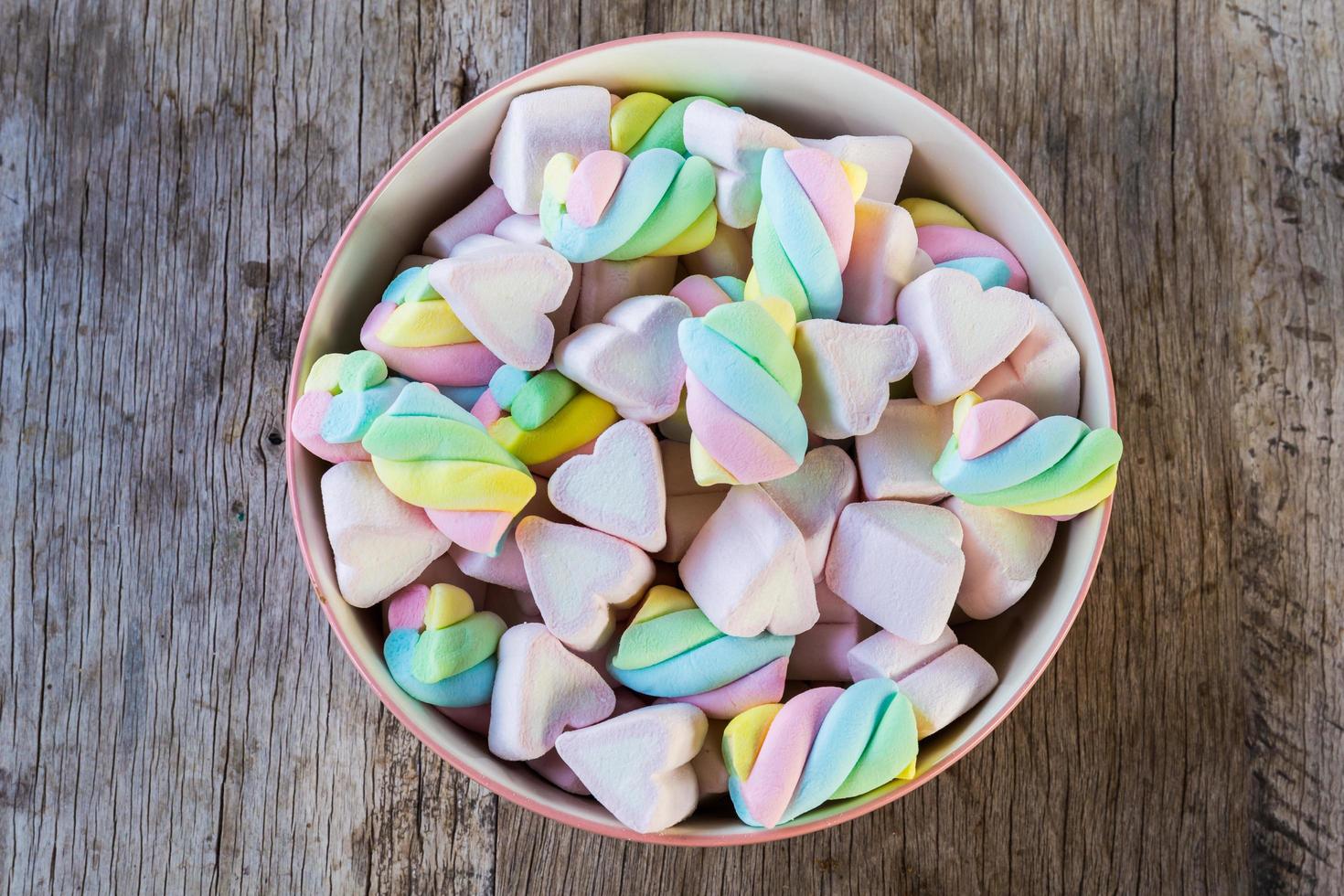 Multi-colored Marshmallow twist and heart in a bowl on a wooden background. Copy space background and texture photo