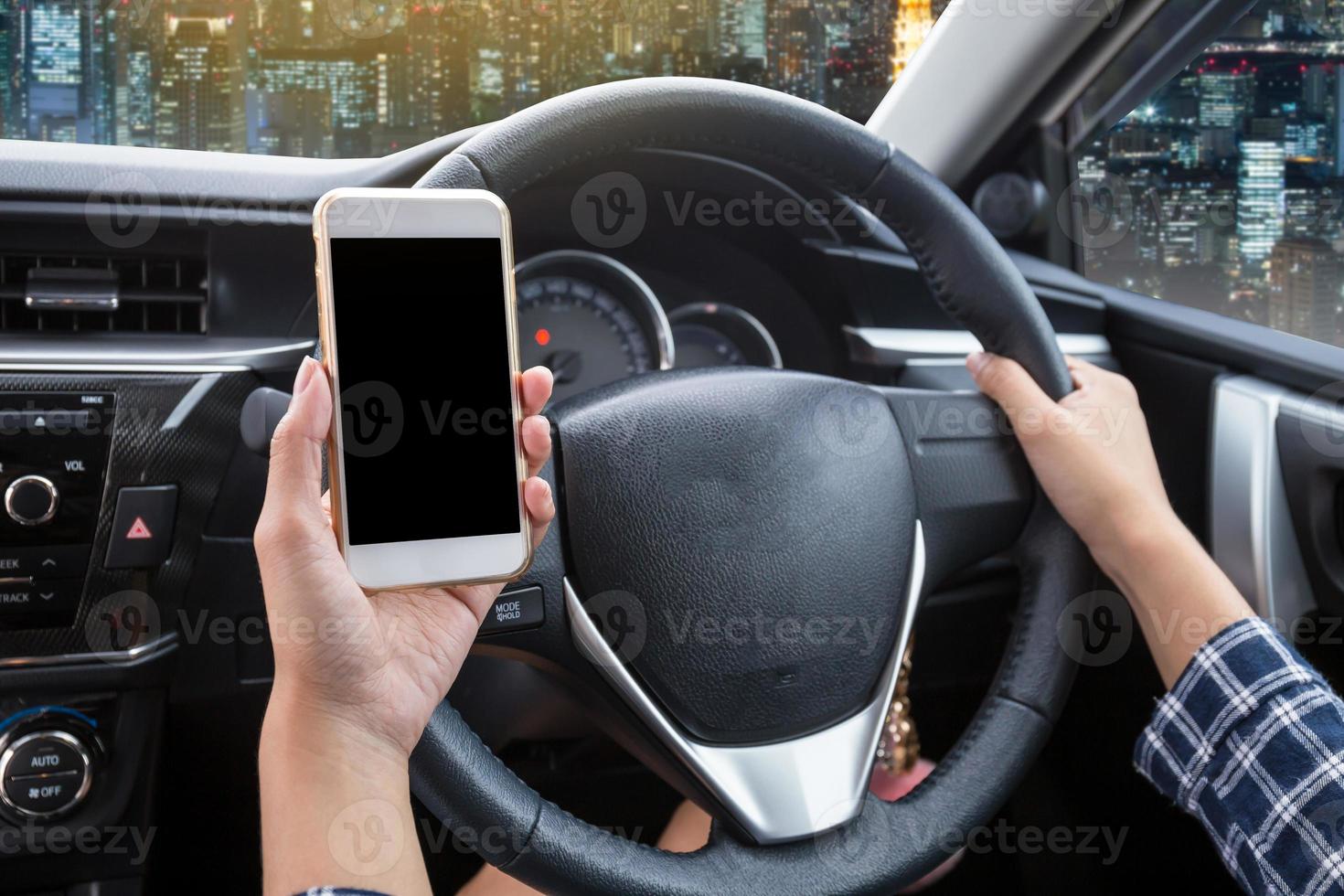Young woman driver using touch screen smartphone and hand holding steering wheel in a car with night city background photo