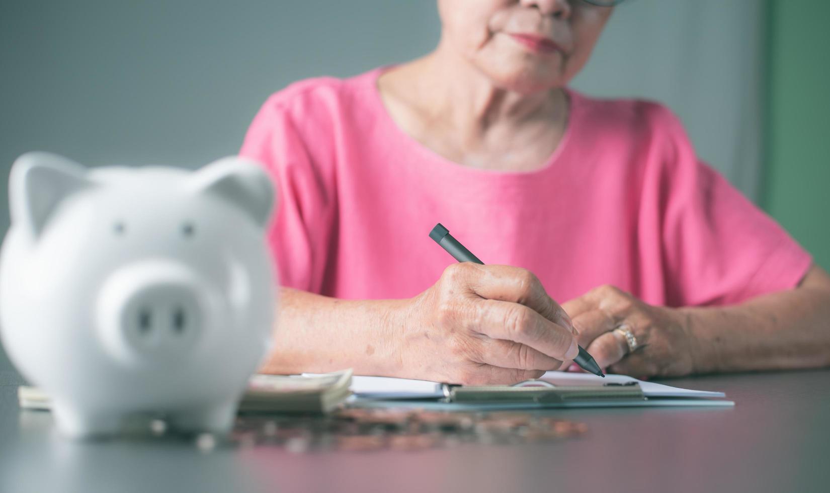 old senior woman sitting down and taking notes on her finances in a notebook. photo