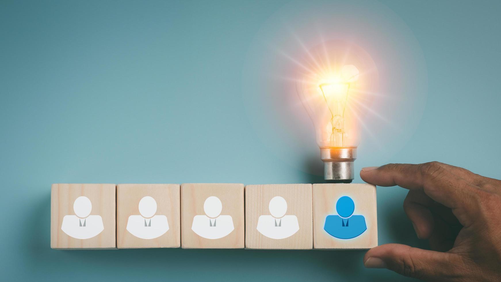 A businessman's hand touches a wooden block. with a light bulb on top, photo