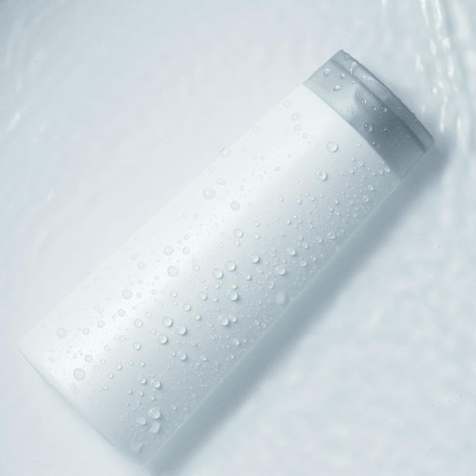 White cosmetic bottle on the water surface. Blank label for branding mock-up. Flat lay, top view. photo