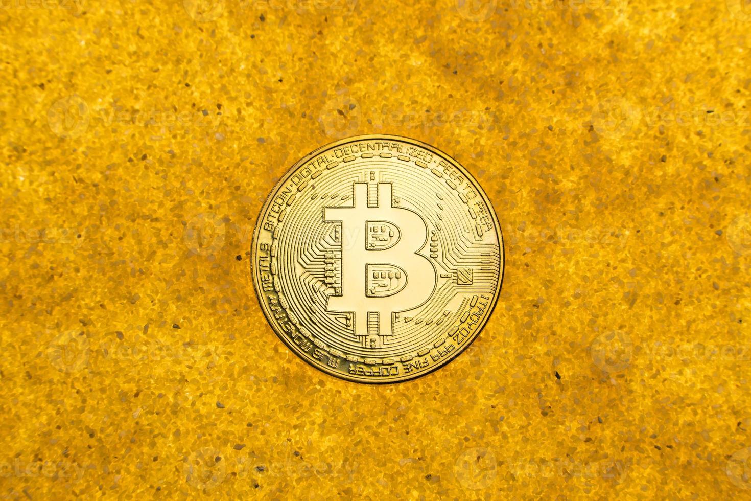 one bitcoin crypto coin on a shiny golden sand background with backlight, top view. photo
