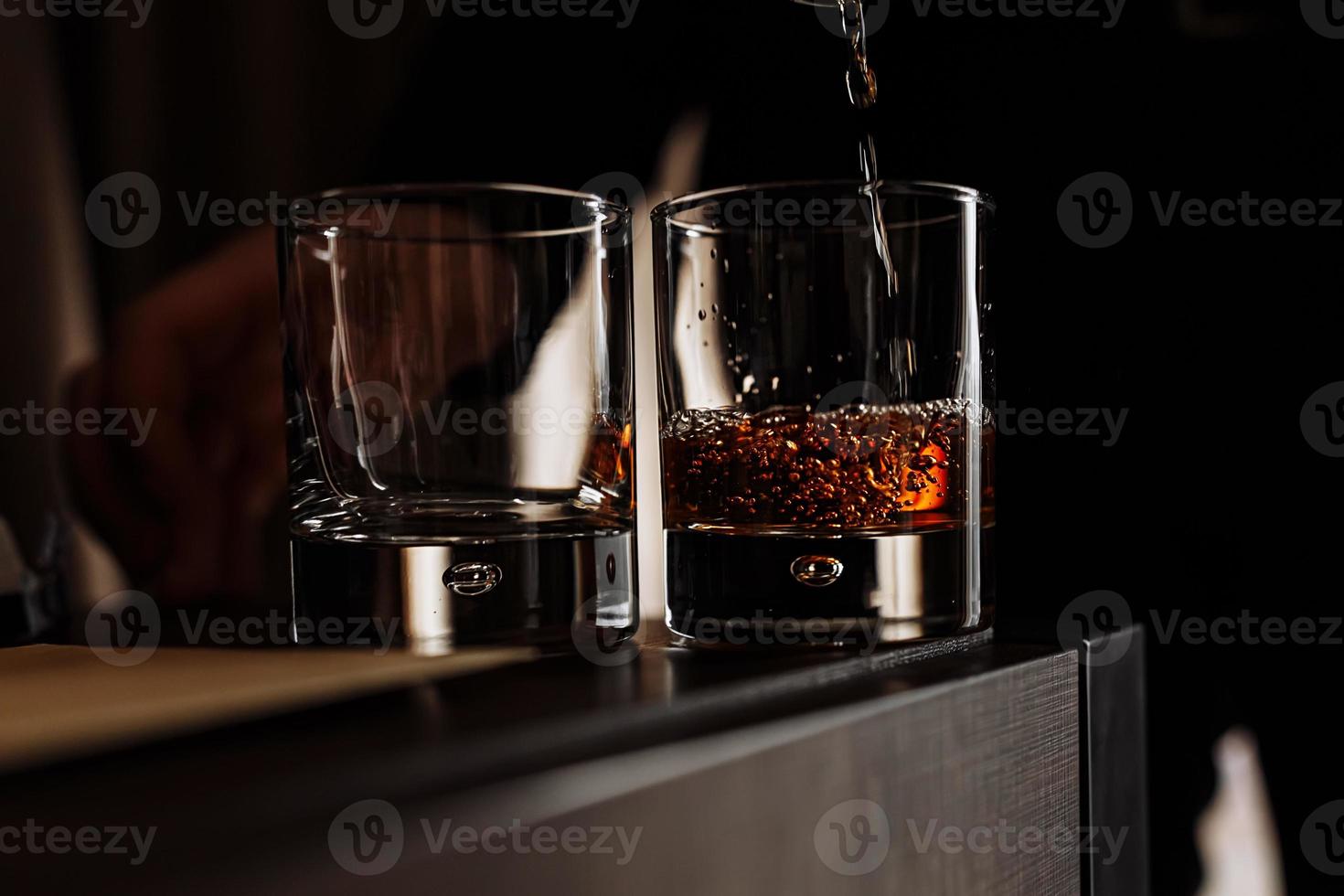 vertiendo whisky de la botella en el vaso de cristal sobre fondo negro. foto