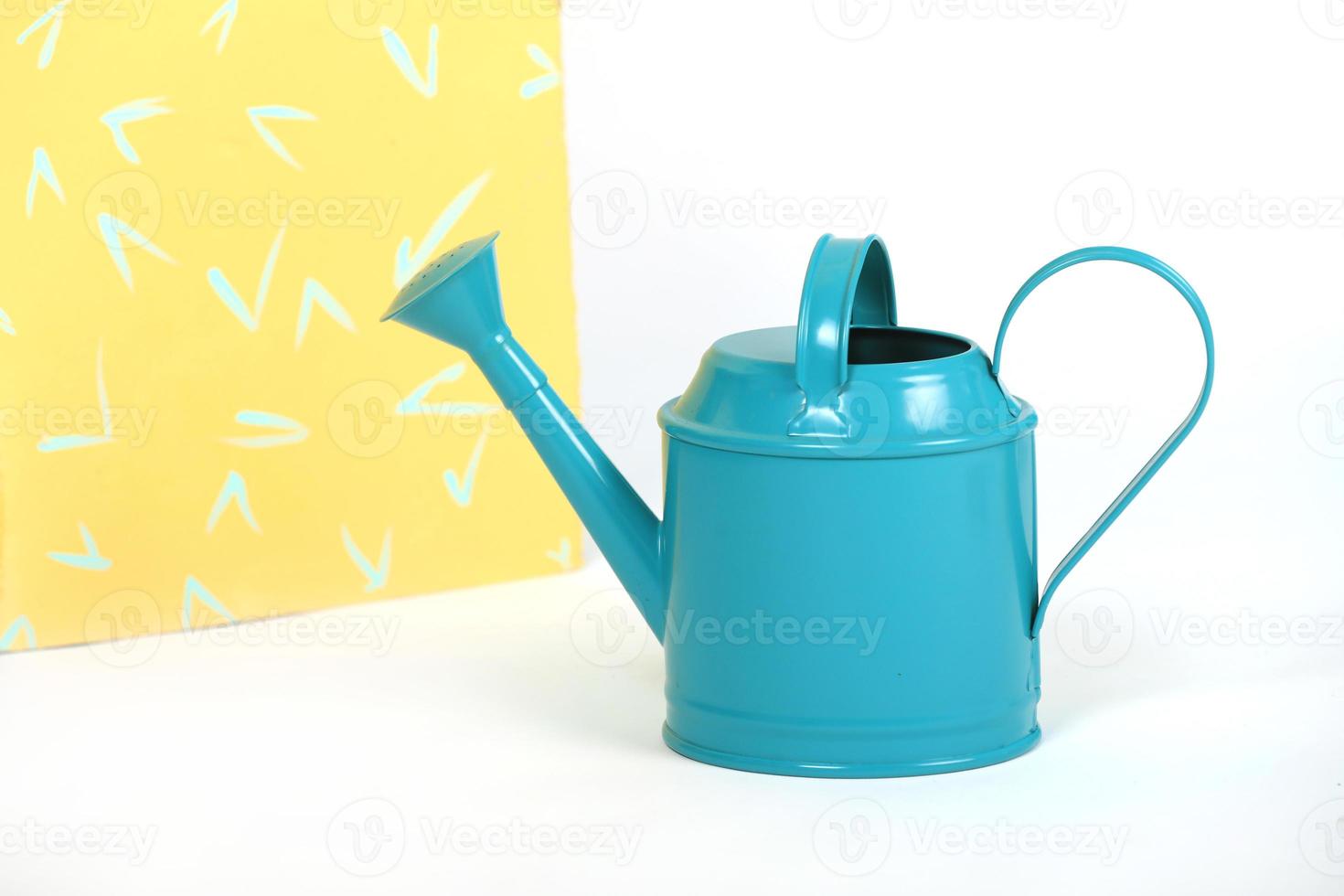 Light blue watering can isolated on white and yellow studio background photo