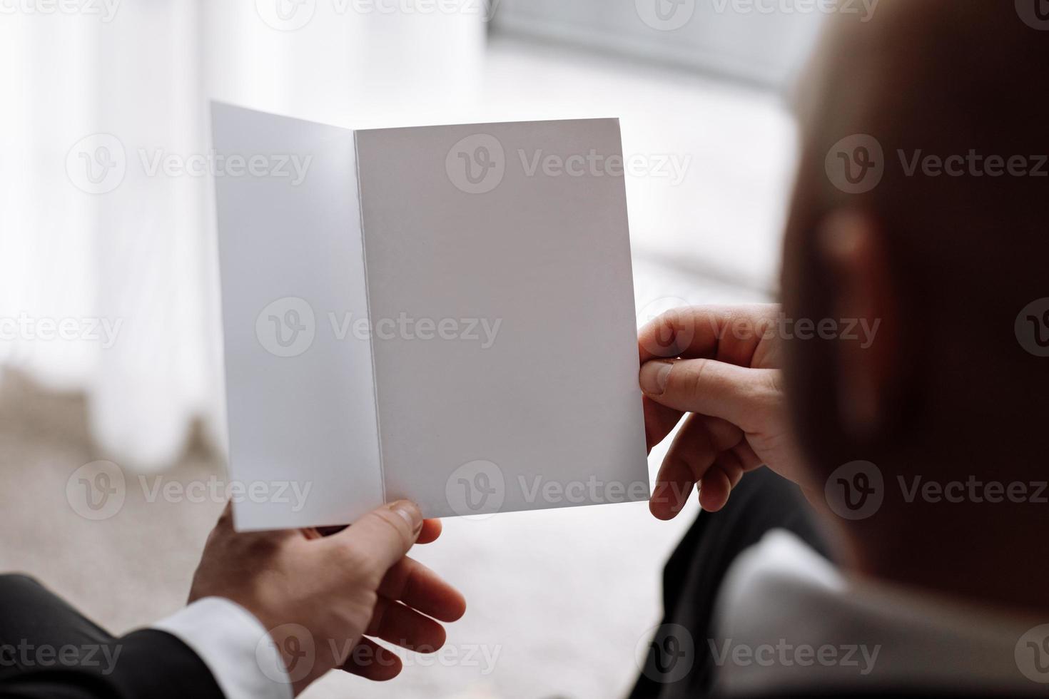 the groom holds an envelope with a letter from the bride. man is reading and sitting in the chair near the window. A letter for the groom. declaration of love. mock up place photo