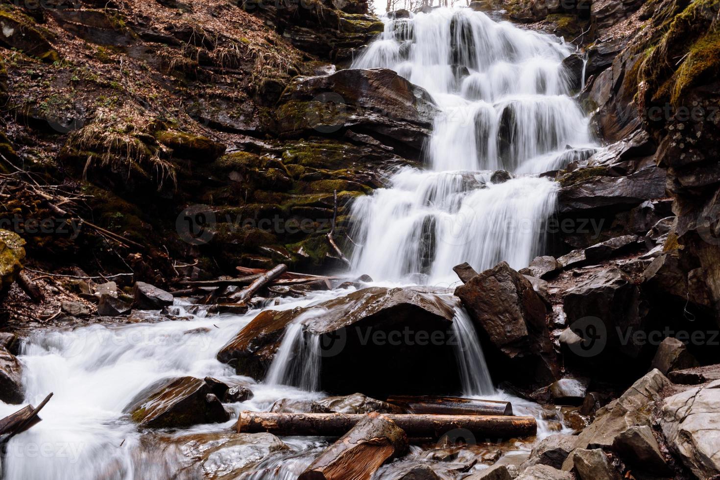 Cascading down a small mountain stream, the water runs over basalt boulders. A small waterfall runs through the moss. photo