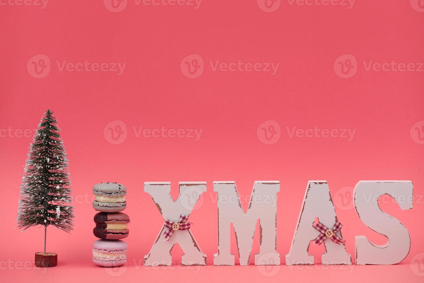 The wooden word xmas with colorful macaroons or macarons and christmas tree on pink background. Xmas decoration. New Year home decor photo
