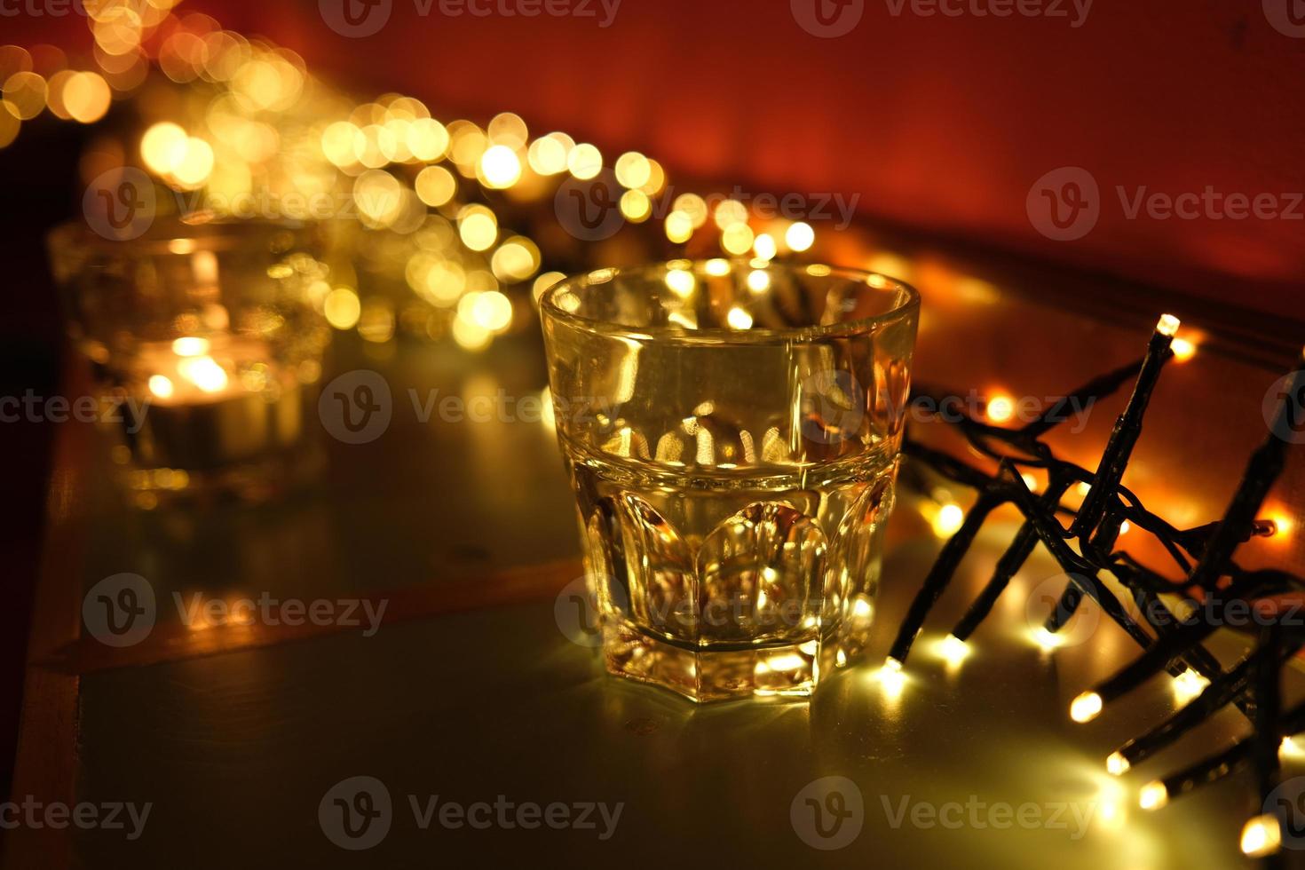 Empty glass in front of blurred Christmas lights on a bar counter. Holiday garlands composition. photo