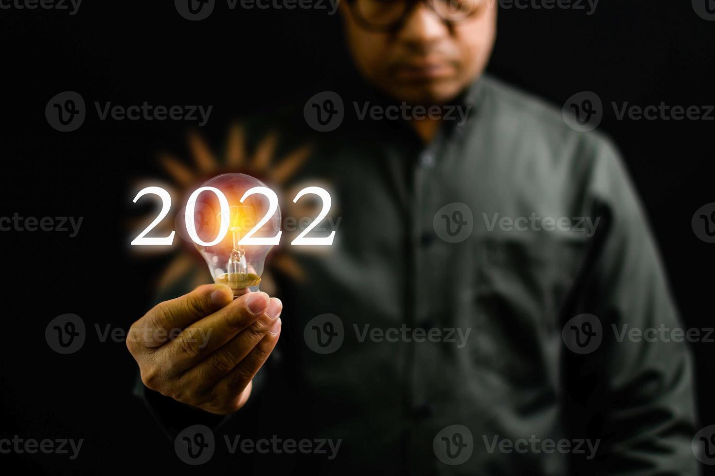 Close-up, A man holding a light bulb is the concept of the startup that drives global business. Bright lights give hope to small businesses. 2022 New Year concept, Copy space, Black Blurred background photo
