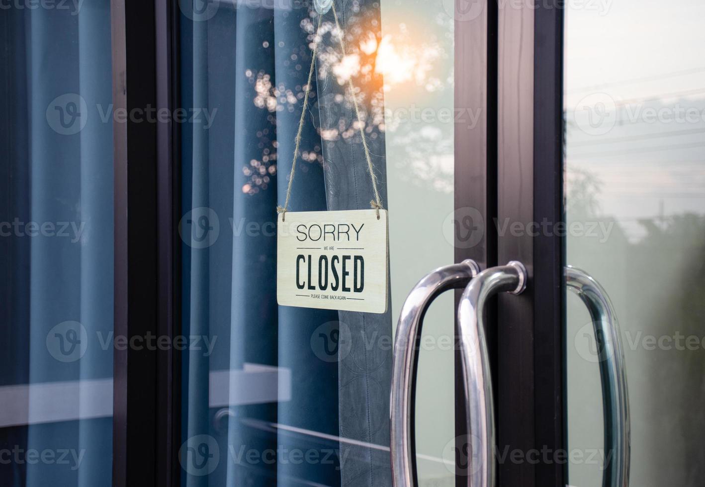 The board hung in front of the glass door of the coffee shop had a message sorry and closed. Light from the soft sun in the morning was bright as the background. Reflection from nature, sky, trees photo